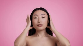Self love and care. Mirror pov portrait of young beautiful asian woman preening, fixing her hair, enjoying her appearance, pink studio background, slow motion