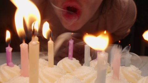 Close up zoom out shot of woman blowing out candles on birthday cake and smiling