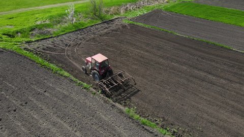 Agricultural red small tractor in the field plowing. System plowing ground on cultivated farm field, pillar of dust trails behind, preparing soil for planting new crop, agriculture concept, top view