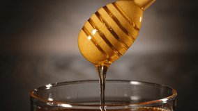 Honey in jar with honey dipper on rustic wooden background. Pouring into the jar. 4k footage
