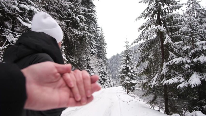 Couple in love walks on a winter road, they hold hands, a beautiful snow-covered forest 