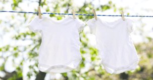 White baby clothes hanging on rope outdoors on spring day