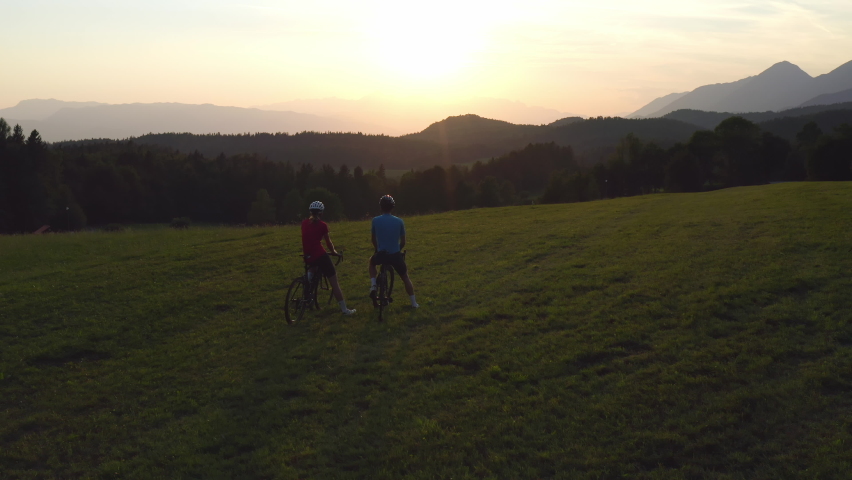 Woman and a man on racing road cycles taking a break after successful training and looking at sunset over mountains giving high five