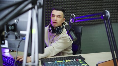 a male radio dj in between broadcasts in a radio studio. the work of a professional host. courses of speech and public speaking.