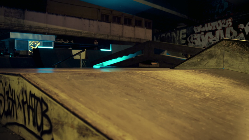 Sporty men training together on ramp at skate park. Active hipster on safety helmet performing stunt on roller skates at night urban skatepark. Healthy lifestyle active leisure enjoyment concept. 