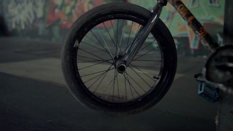 Bmx bicycle wheel spinning at skatepark with graffiti wall. Closeup brown bmx bicycle gear at skate park. Close up bike parking against ramp outdoors. Extreme sport transportation cycling concept. 
