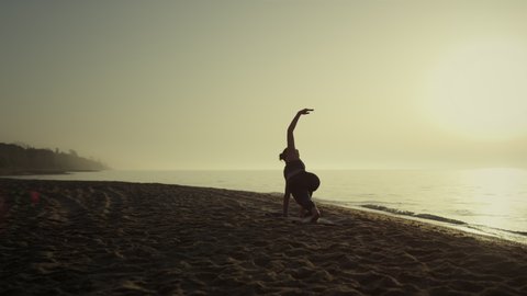 Yoga woman exercising on beach enjoying beautiful morning sunrise. Sporty young girl making plank pose raising hand outdoors. Slim sportswoman stretching on sand seacoast at summer. Sport life concept