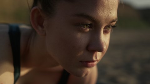 Attractive woman face looking forward on sand seacoast close up. Portrait of beautiful girl training enjoying calm sunset summer evening. Pretty lady meditating on beach outdoors. Healthy lifestyle.