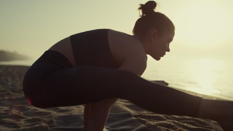 Athletic woman standing on arms spreading legs to sides practicing yoga close up. Attractive girl making tittibhasana wearing sportswear at sunset outdoors. Sportswoman workouting flexibility outside.