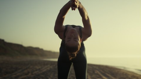 Attractive girl pulling arms back practicing bridge pose at sunset close up. Flexible woman making yoga stretching on sand beach. Young sportswoman training balance bending body outside. Sport concept