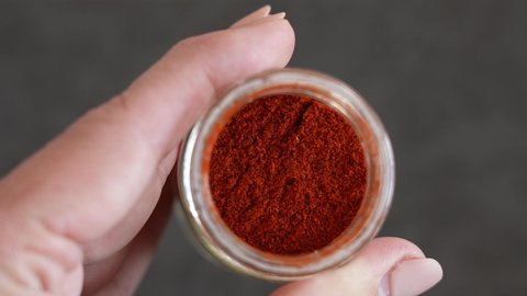 Closeup view 4k stock video footage of grounded into powder red smoked paprika pepper isolated in glass container. Woman holding glass bottle full of fry grounded powder red pepper spices