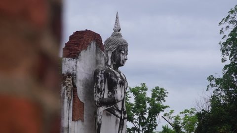 PHITSANULOK, THAILAND – MAY 02, 2022: A Buddha statue standing with background of a laterite wall near Nan river at Chan Palace of King Naresuan the Great in Phitsanulok province of Thailand.