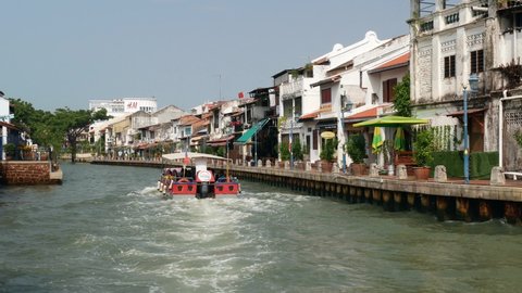 Malacca, Malaysia - May 5,2022:  Riverside scenery of a cruise full of passengers crossing by the Malacca River. It has been listed as UNESCO World Heritage Site since 7 July 2008. 
