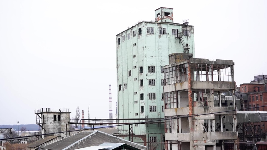 An old, abandoned, commercial building with industrial chimneys in the background.