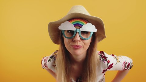 young blonde woman with rainbow sunglasses looking into the camera medium closeup studio shot orange bakground. High quality 4k footage