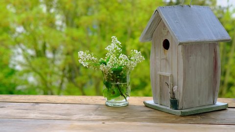 sprigs of white bird cherry, birdhouse is ready for new spring season, house against the background of spring green foliage of trees, concept of bird housewarming, helping animals, basis for designer