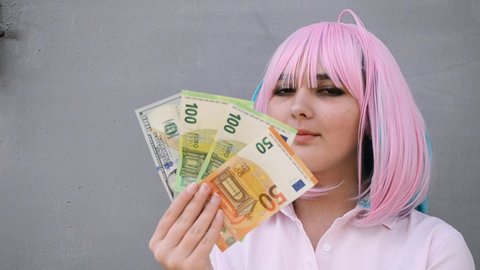 Girl in pink shirt and with pink color hair holding cash money euro and dollars. Bank staff portrait, anime girl cosplay