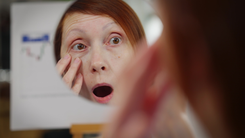 Close-up reflection in mirror of anxious mature Caucasian woman touching wrinkles. Worried lady sitting in office checking face skin. Aging and femininity concept Royalty-Free Stock Footage #1089907659
