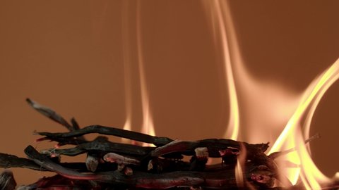 The wooden fire is orange, and the smoke of the fire from the mustard tree is on a brown background. Close-up of a flame with white smoke. Slow motion, 4K.