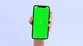 Rotation phone with blank green screen vertical and horizontal in woman hand, demonstrating copy space for app or website design, standing over blue studio background, mockup footage.