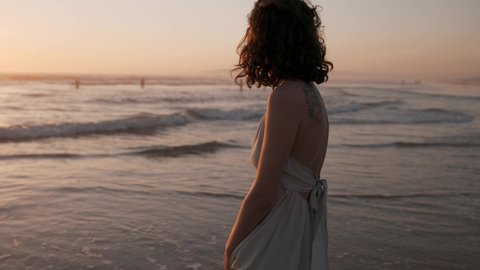 The beautiful young woman walks by the ocean at sunset.