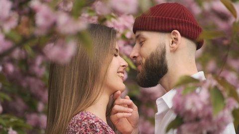 Romance, kiss, couple, sakura. Young couple in love outdoor. Sensual outdoor portrait of young stylish fashion couple. Couple lovers hugging and kissing in the park. Love, youth, happiness concept