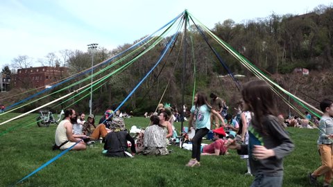 Pittsburgh, PA USA. April 30, 2022. Children running around a may pole while adults are seen talking  underneath and eating a picnic lunch in the Polish Hill neighborhood of Pittsburgh.