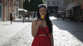Young beauty woman in red dress is smiling and eating ice cream during walking in the street of historical part of Bratislava city in sunny summer afternoon in Slow Motion HD VIDEO. Half speed. 