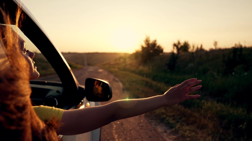 Happy girl in car window. Hair in wind. Girl travels by car. Hand in sun. Windy breeze from car window. Happy girl smiling from car window. Windy breeze in your hair. Hand in the rays of the sun | Shutterstock HD Video #1089918023