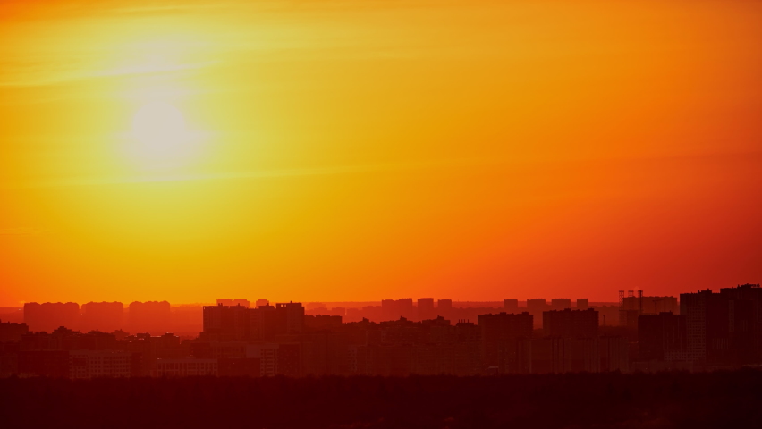 Sunset on a red sky with evening clouds in the city, timelapse. The setting evening sun over the city with high-rise buildings