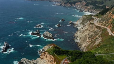Wide aerial view of the winding curvy highway road along Route 1 on the coast of Big Sur California with waves crashing into the large rocks in the Pacific Ocean