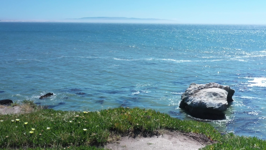 Walking along a bluff overlooking the ocean then panning to view a huge rock along the shore