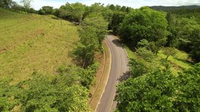 AERIAL: SUV car driving through road bend while travelling in exotic countryside. Winding asphalt road in tropical location. Driving along asphalt road through lush green landscape.
