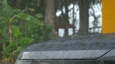 STILL SHOT, CLOSE UP: Pouring rain and bouncing raindrops on the gray car hood. Overlooking tropic cloudburst and dripping raindrops on car hood. Moody weather during wet season at exotic location.