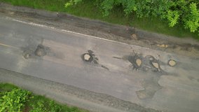 AERIAL TOP DOWN: Car driving over big road pits on countryside road in tropics. Careful drive while travelling along countryside road in tropical destination. Bad road maintenance in third world.