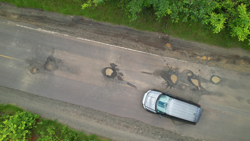 AERIAL TOP DOWN: Car driving over big road pits on countryside road in tropics. Careful drive while travelling along countryside road in tropical destination. Bad road maintenance in third world. | Shutterstock HD Video #1089920829