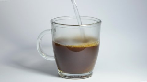 A man brews morning coffee with boiling water close-up. An overhead view of a mug of instant coffee standing on a white table into which a stream of hot water begins to flow.