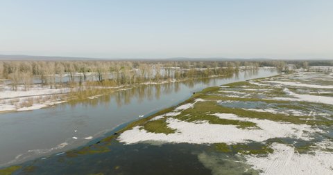 Flooded river floodplain with snow field and forest in wild lanscape. High altitude wide drone view flooded area at spring time cloudy day