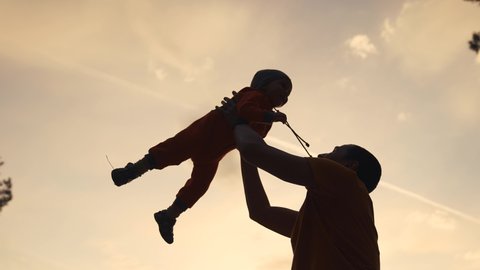 father play with his baby son in the park. happy family kid dreams people silhouette concept. father plays with baby son throws up a silhouette against the sky in a city fun park. happy family