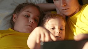 happy family at home. mom baby son and daughter watching online video on a smartphone gadget lying in bed at home. sunlight from window morning. happy family online video chat fun mom and baby kids