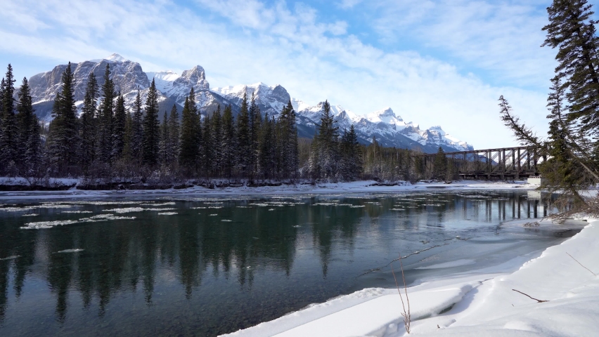 Canadian Rockies beautiful scenery in early winter. Drift ice floating on Bow River, snow capped Mount Rundle mountain range reflections. Canmore, Alberta, Canada. Royalty-Free Stock Footage #1089925351