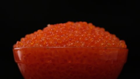 Red caviar. Bowls with red salmon salted roe caviar on tasting table. Hands pick caviar in spoon. Expensive healthy food concept on black background close-up slow motion rotate