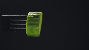 A fork with a cucumber on a dark background is poured with olive oil.slow motion.vertical video
