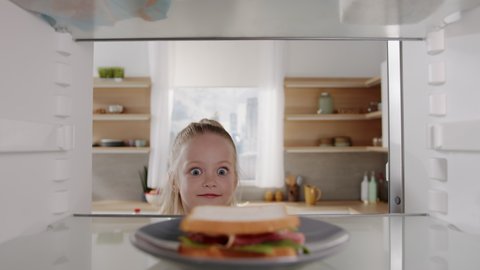 Pretty caucasian girl opens fridge door and taking out tasty sandwich. Little hungry girl looking for food in an empty fridge. POV from inside the refrigerator.