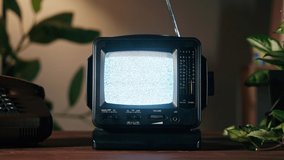 Small old television with grey interference screen on home background. Close-up of vintage tv on table with retro phone and plants, nostalgia. 