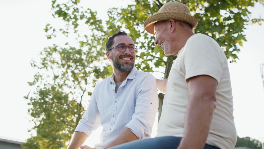 Happy senior man with his mature son sitting on stairs in park.