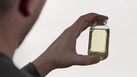 A man holds a small glass jar in his hand. There is a yellow liquid in the vessel. 
