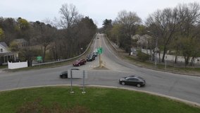 Static drone clip of traffic navigating a rotary and some offshoot roadways. View up a long hill. Cloudy.