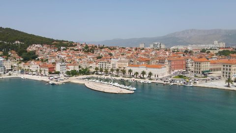 Aerial drone forwarding shot showing ancient roman town beside blue sea and mountains iin the background in Split, Croatia on a bright sunny day.