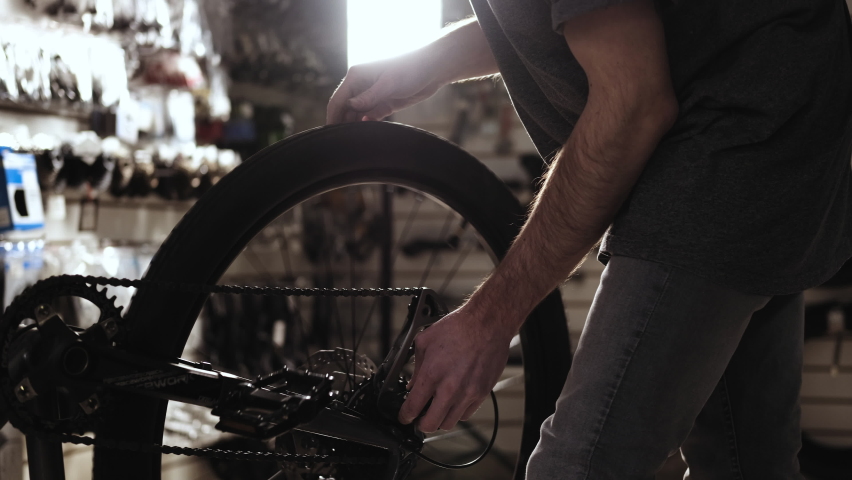 Bicycle wheel repair. man works in workshop. Caucasian master of service turns wheel and checks tension of chain. bicycle repair small businesses.  service center for the repair of sports equipment